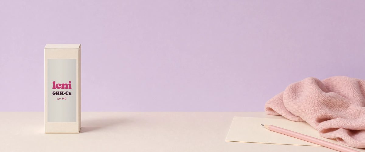A Leni carton, a blank note card and a pink pencil on a cream surface against a lilac wall.